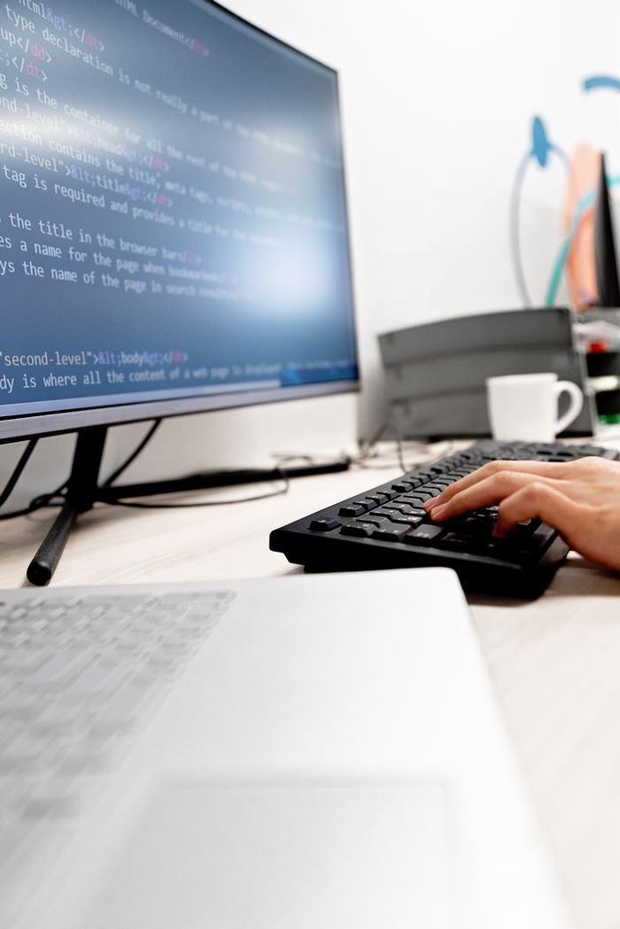 Home Close-up of hands typing code on a computer monitor in an office setting.
